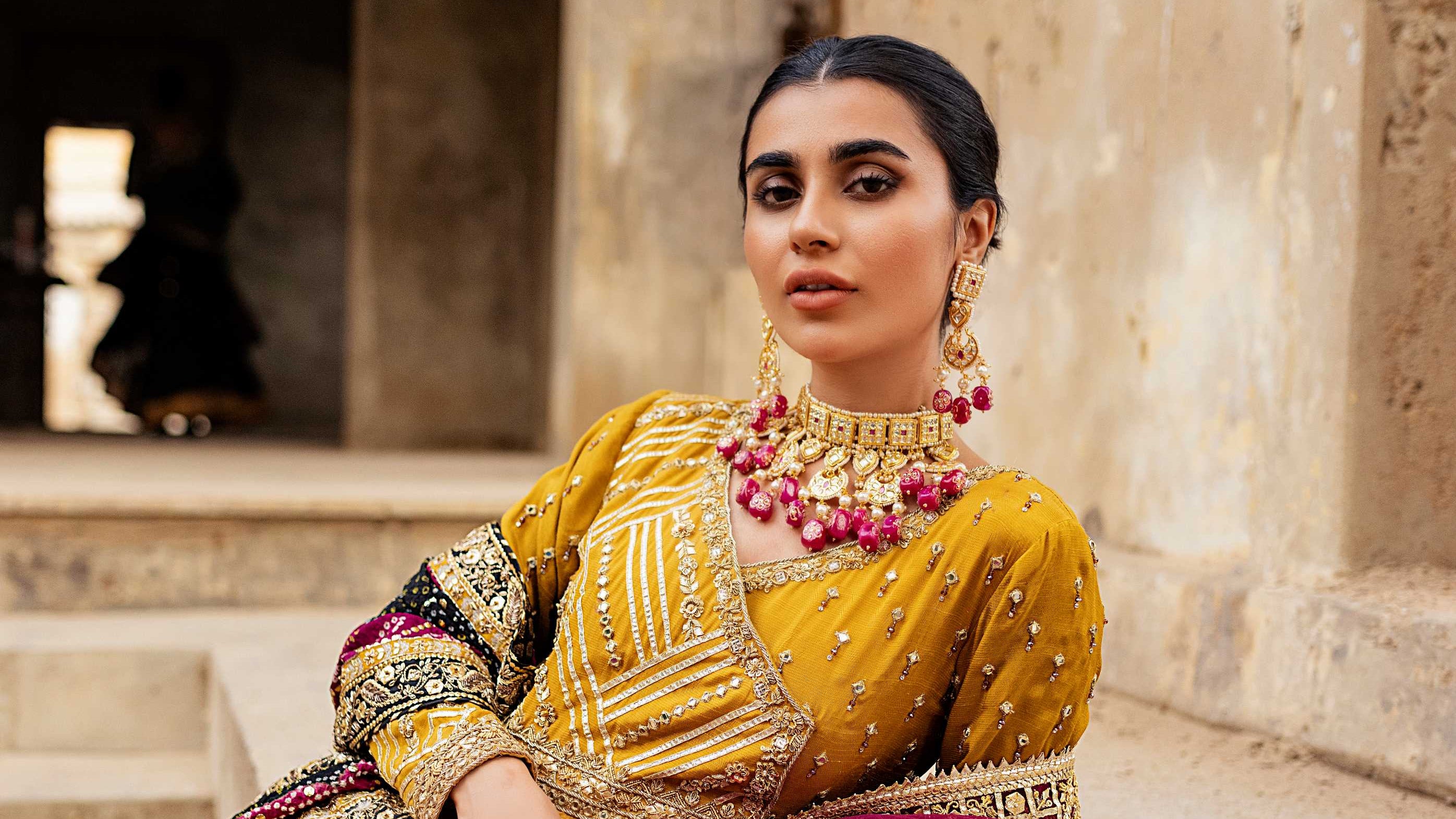 Woman in traditional yellow and pink outfit with jewelry sitting on steps.