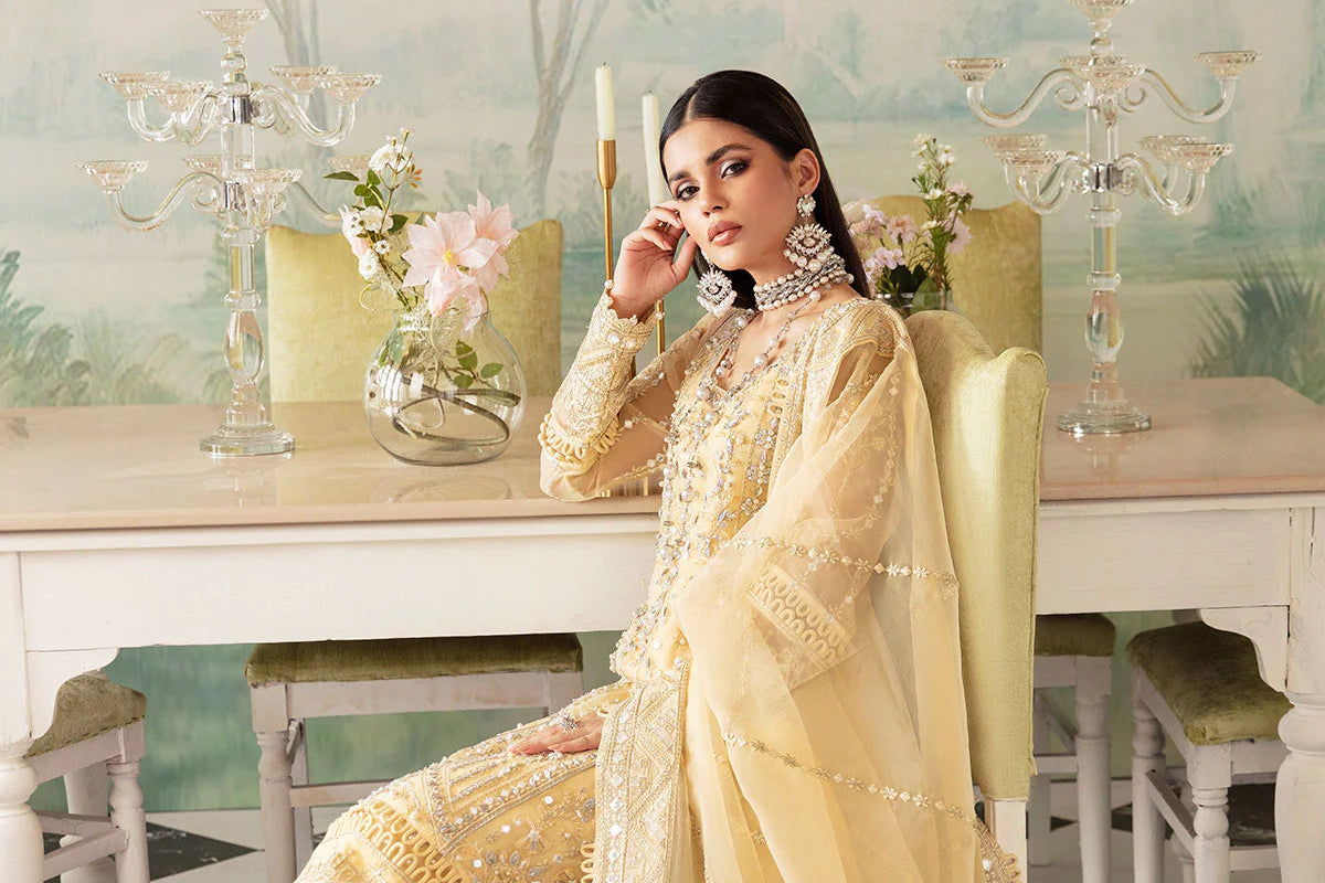 Woman in a beige embroidered traditional outfit sitting in a decorated room.